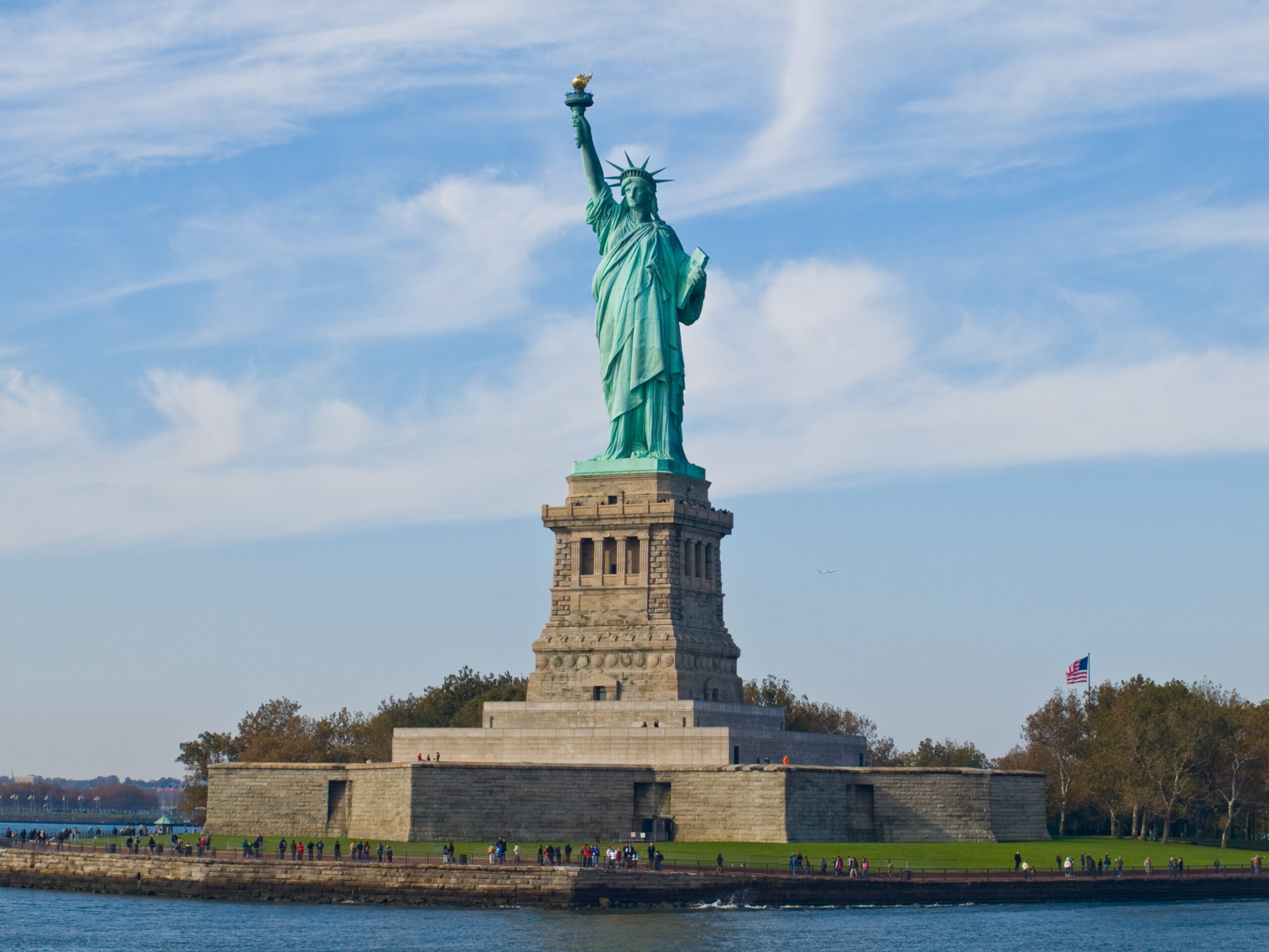 Statue of Liberty stands tall, holding a torch against a clear blue sky. Visitors admire the iconic symbol of freedom and democracy.